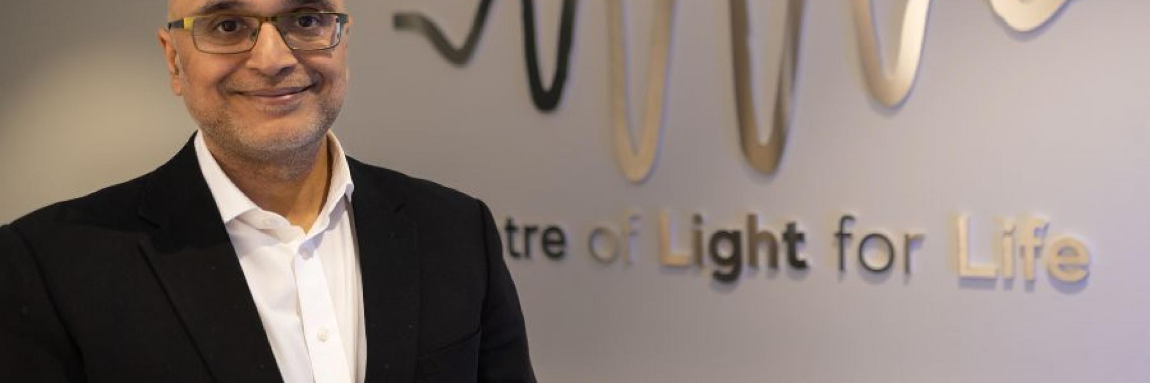 Prof Kishan Dholakia in front of the Centre of Light for Life's logo