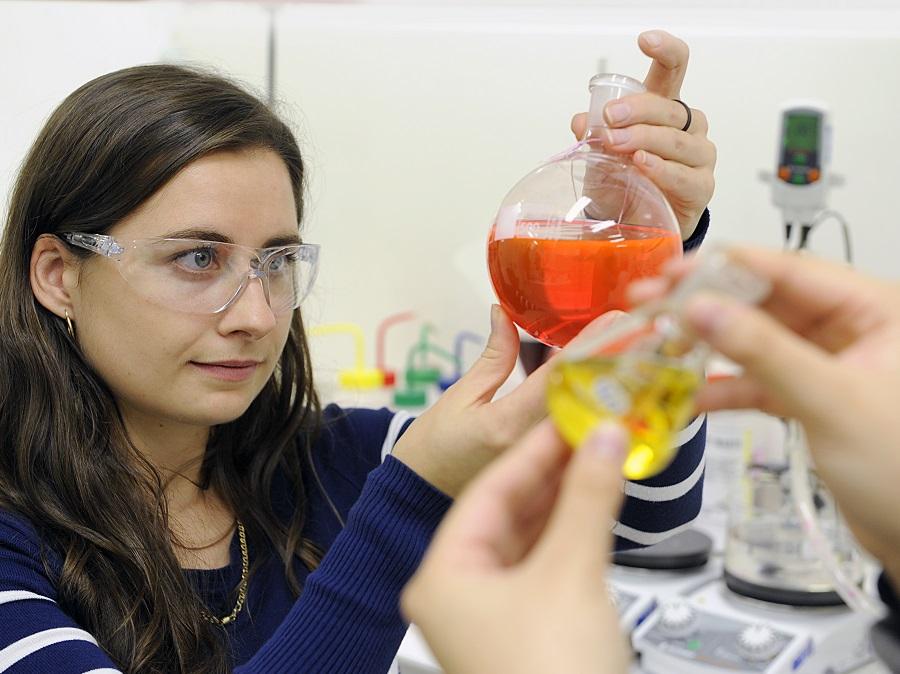 PhD student observes a vial containing orange liquid