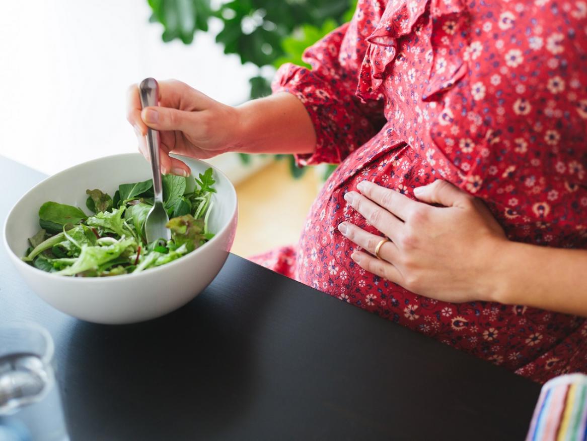 A pregnant woman eats a salad.