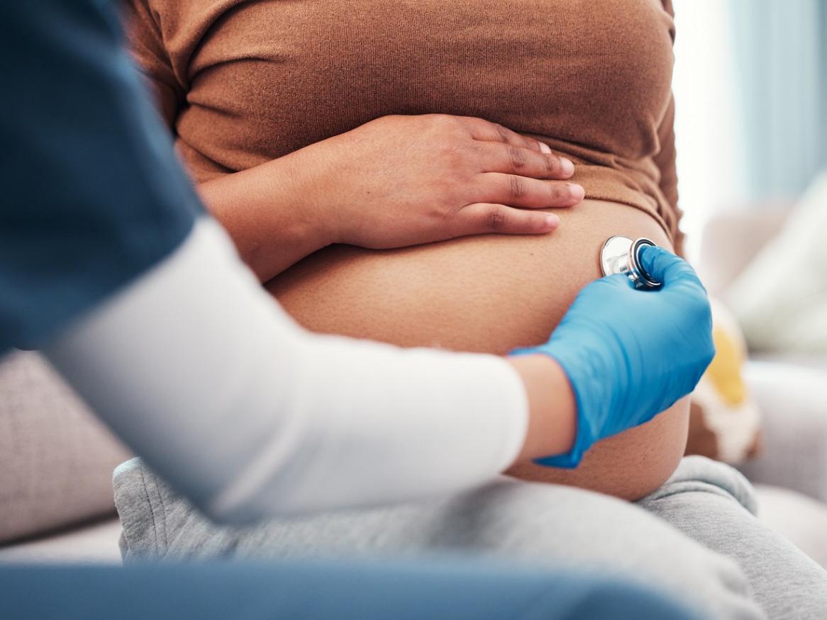 Health professional holding stethoscope on pregnant woman's stomach.