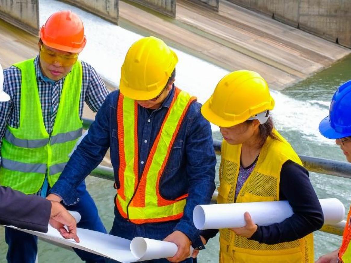 Staff in high-vis clothing, looking at plans, near water