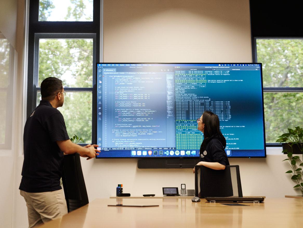 people in meeting room looking at a large screen with computer code