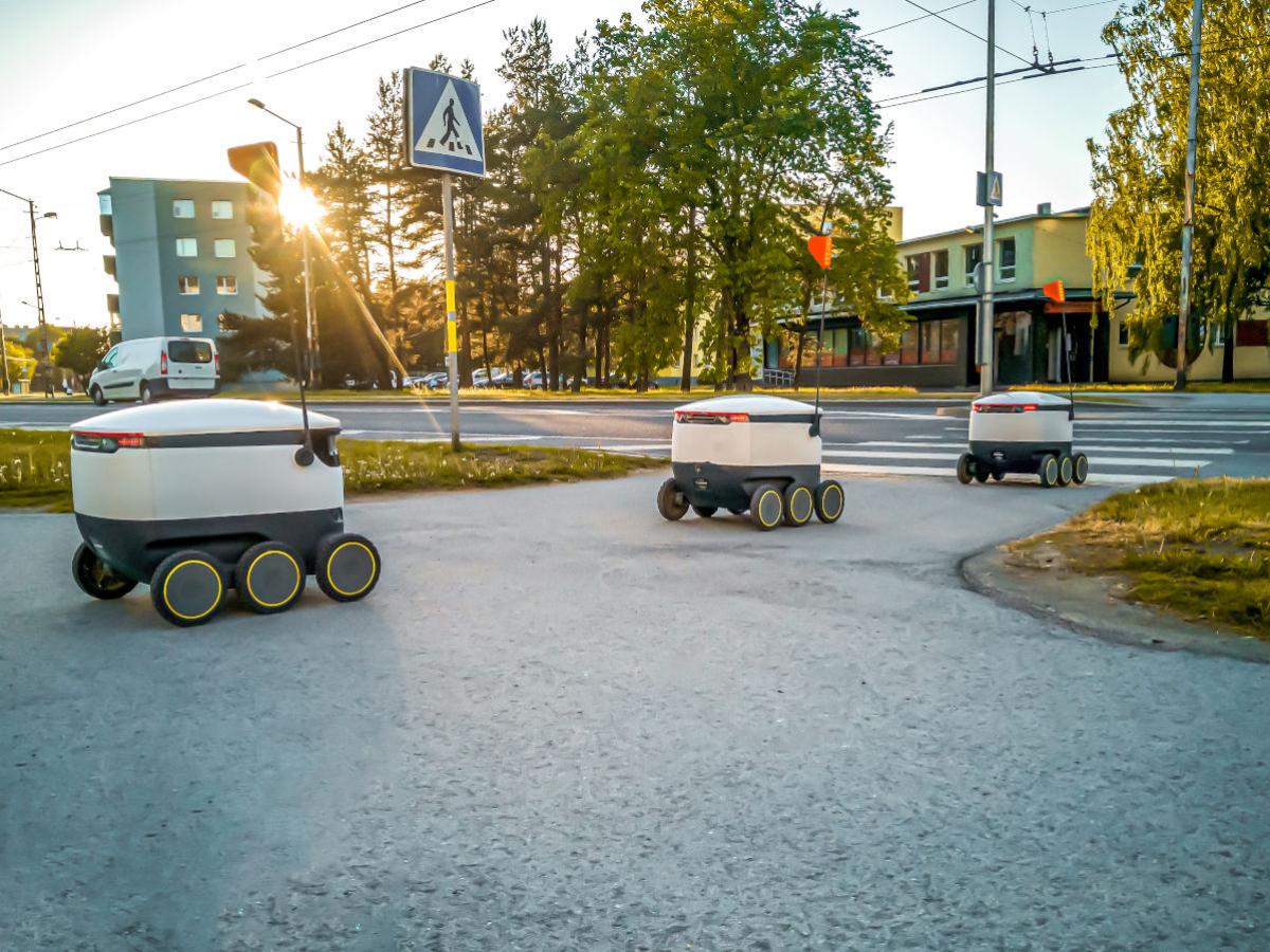 three small autonomous delivery vehicles cross a street
