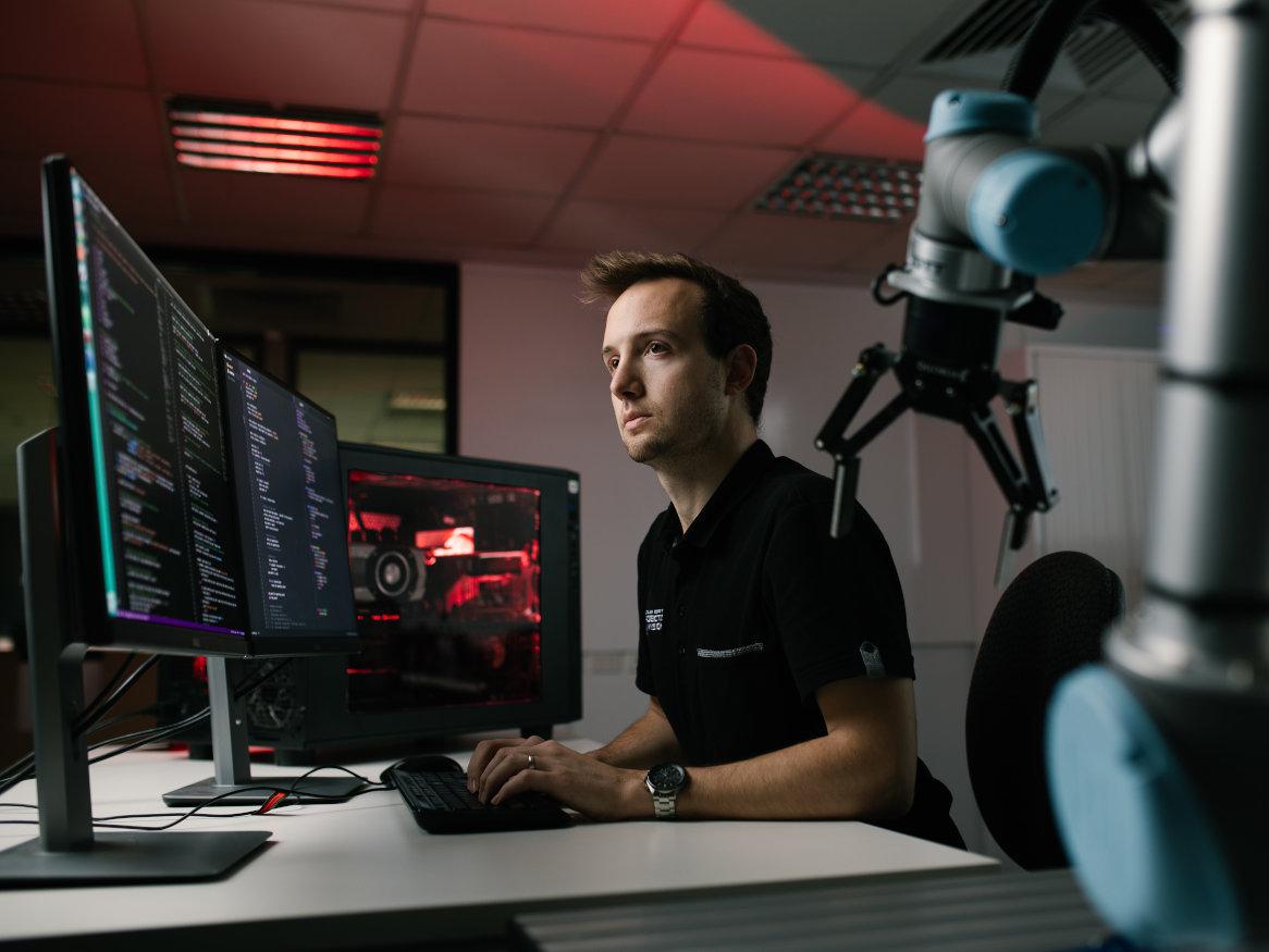 young man working at a computer terminal with a robot arm attached to desk