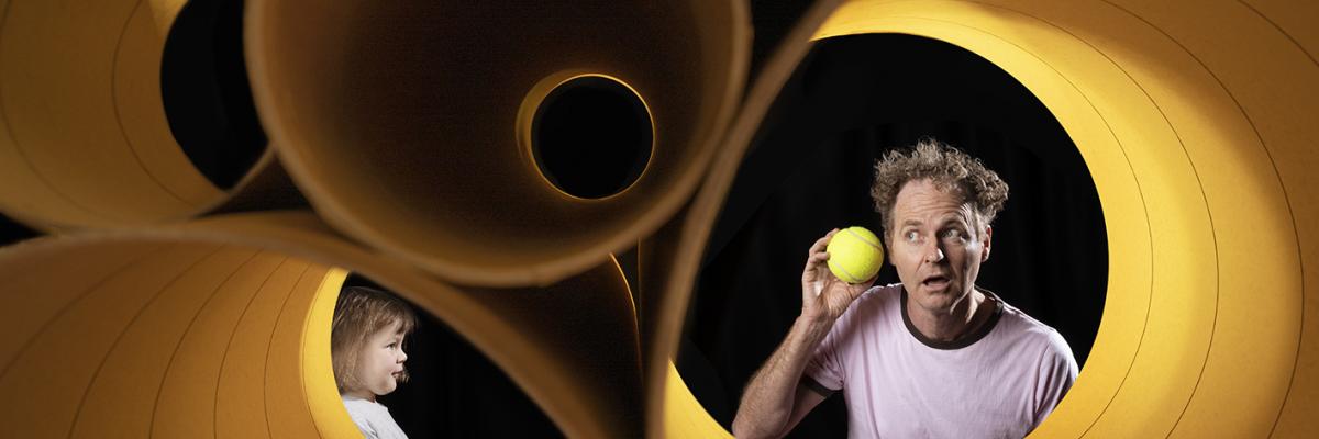 Stephen Noonan on set with large yellow cylinders and a ball