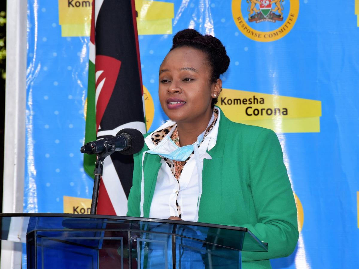 Dr Mercy Mwangangi giving a speech from a lectern with flags behind