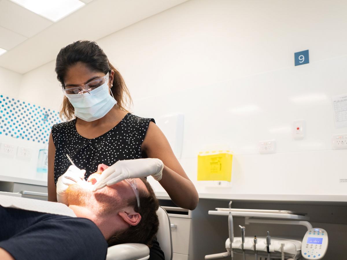 Dr Kumarasinghe wearing a mask and gloves, working with a patient