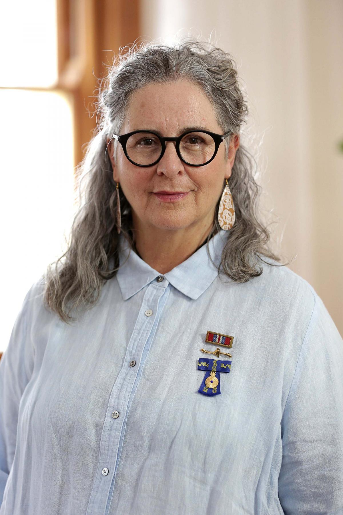 A portrait of Lesley Salem AM in a blue shirt and glasses