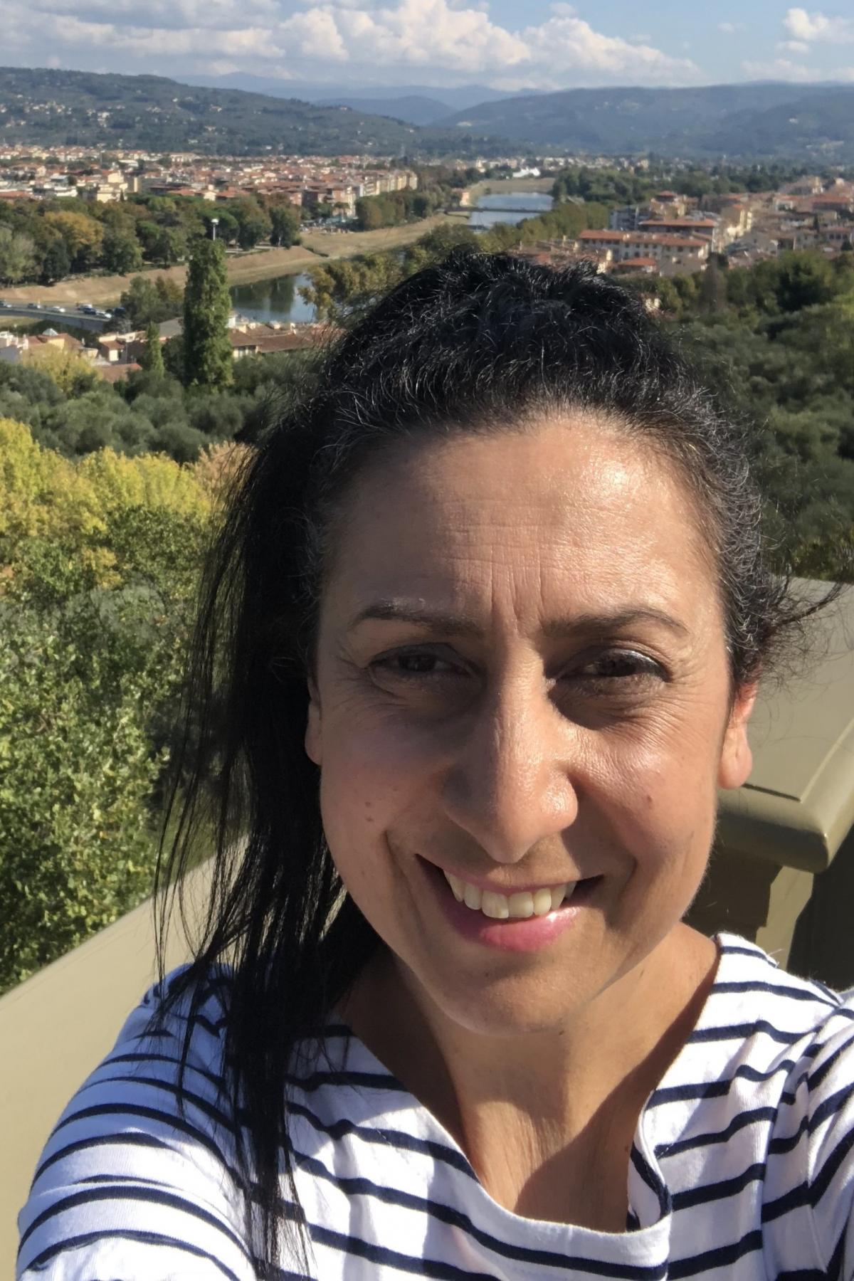Christine Economos smiling at the camera, a beautiful greek landscape behind her