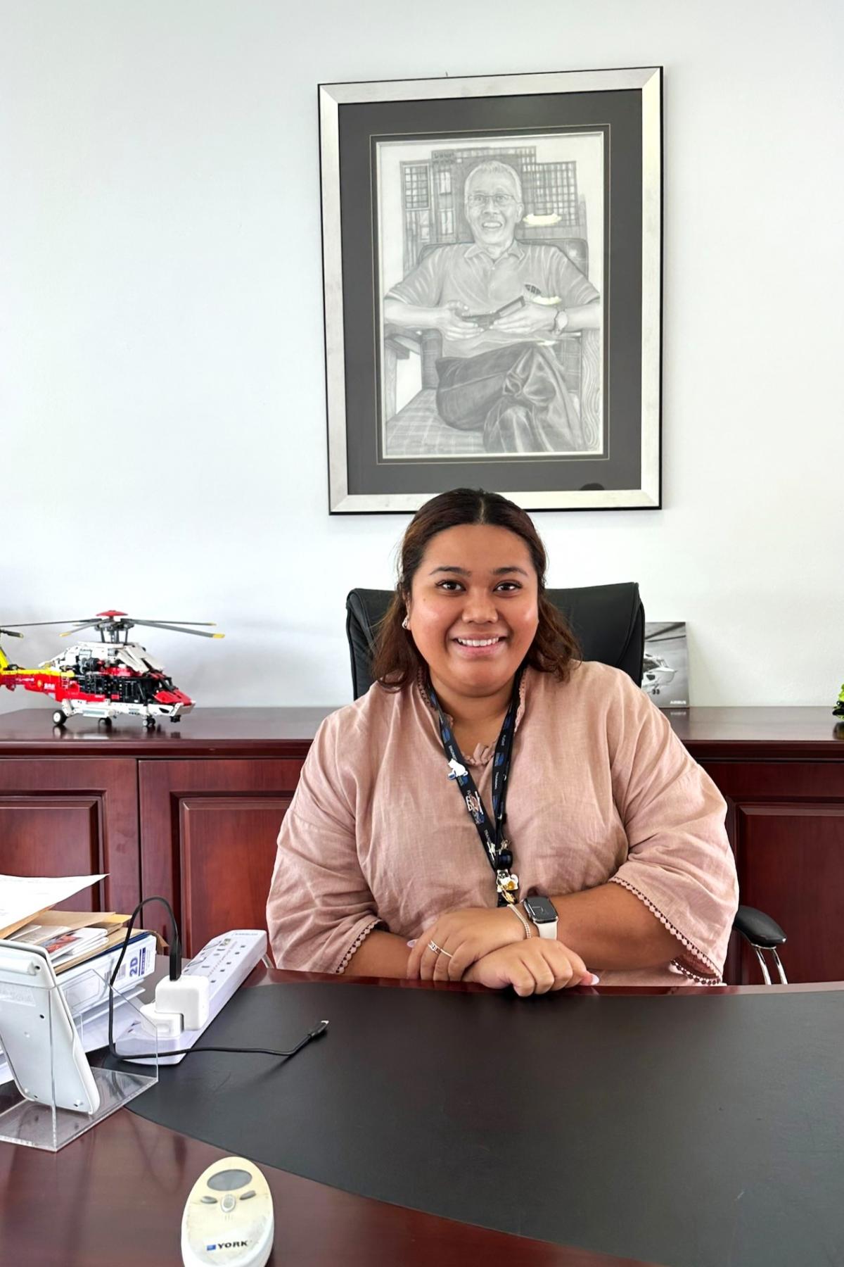 Ida sits at her desk below a portrait of her father