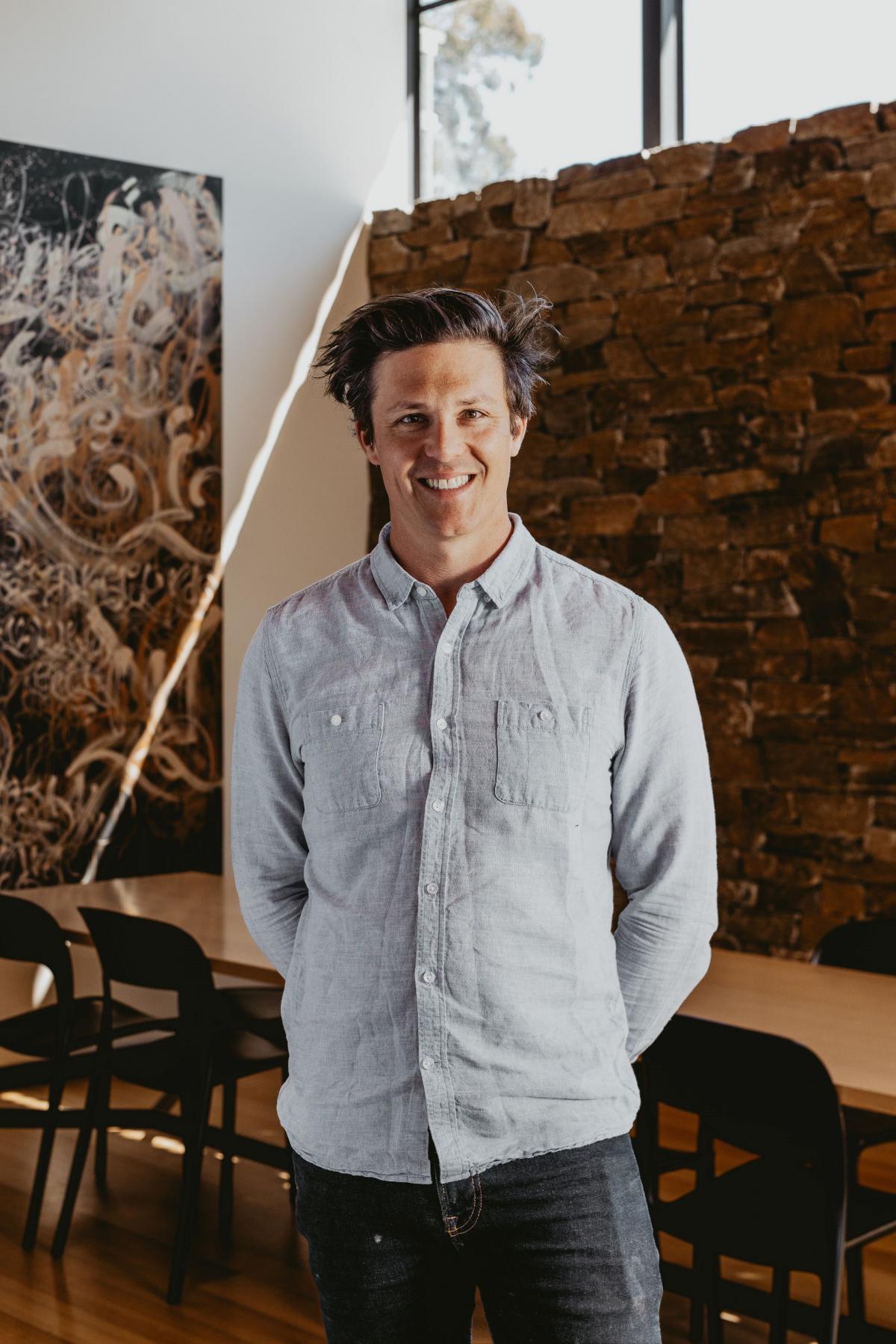 A portrait of Chris in a blue shirt in a spacious room