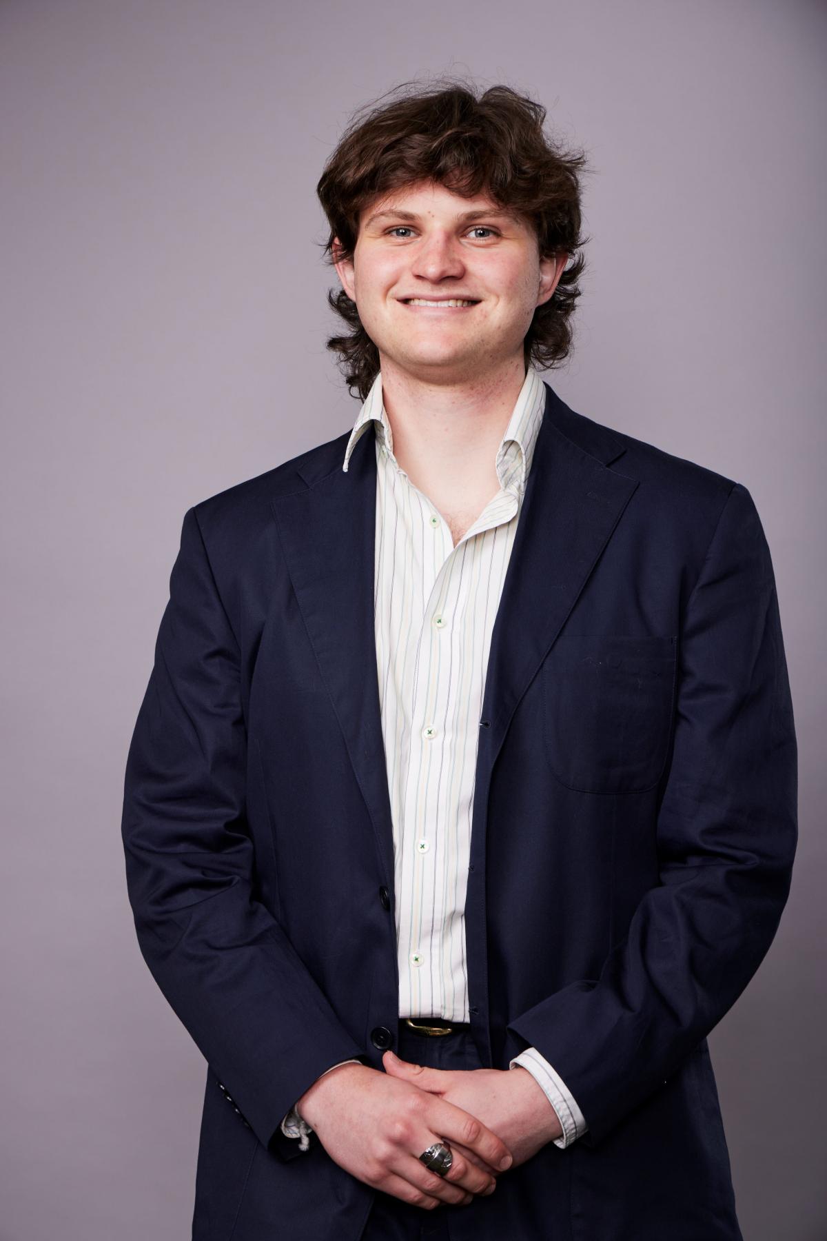 A portrait of Harry smiling, wearing a navy suit