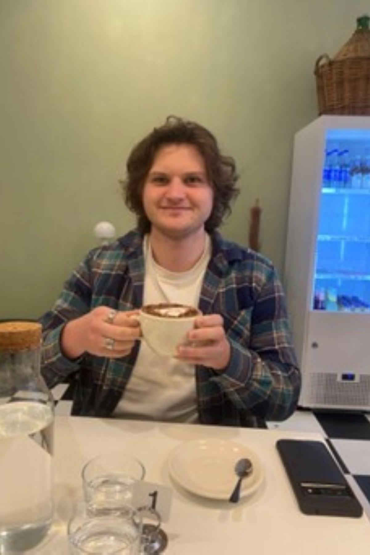 Harry sitting at a table with a cup of coffee, a fridge behind