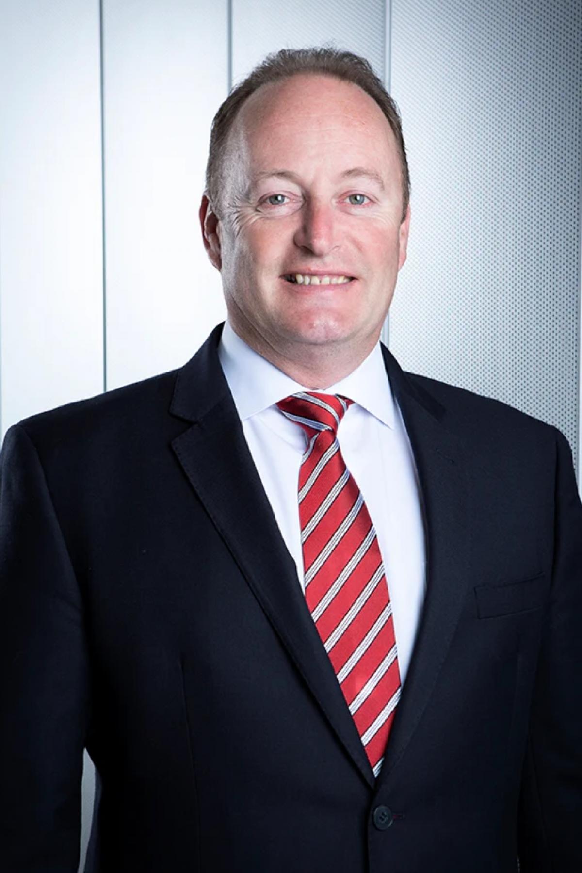 A portrait of Rob Chapman in a suit and red tie, smiling