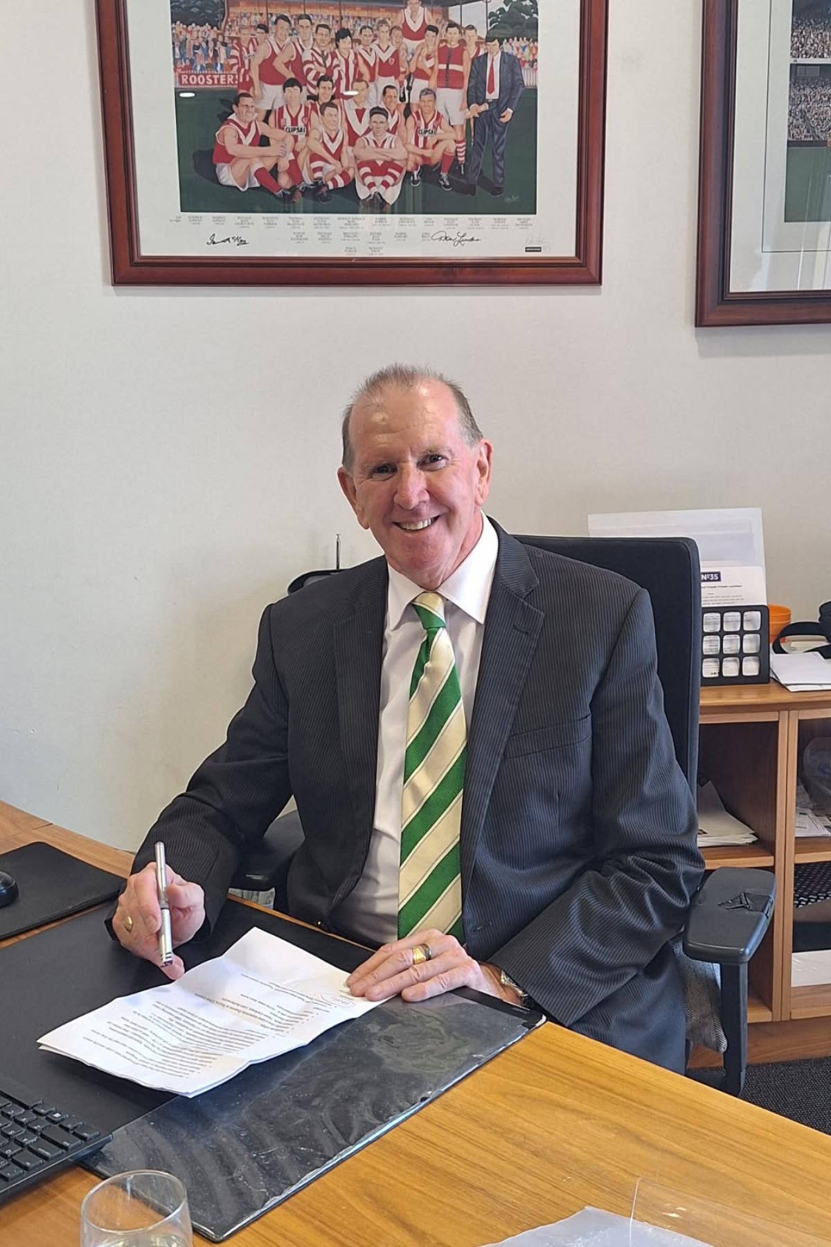 Peter Anderson in a suit and tie, smiling while sitting at his desk