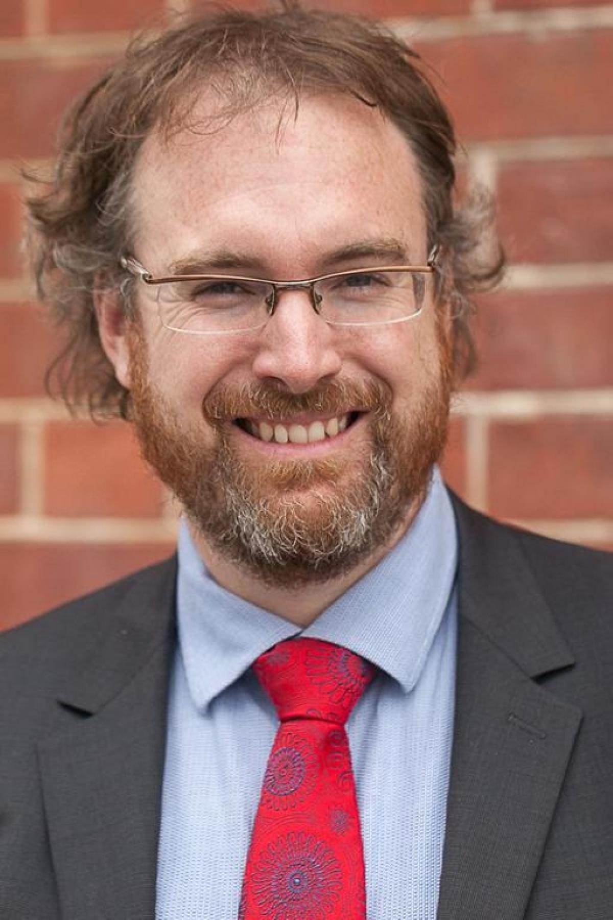 A portrait of Joe McIntyre smiling in front of a brick wall