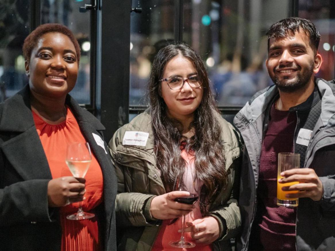 Three students standing with drinks at the winter warmer event 2022
