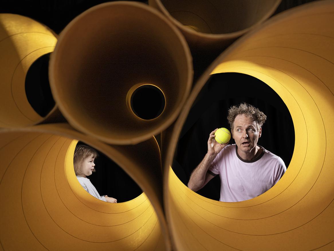 Stephen Noonan on set with large yellow cylinders and a ball