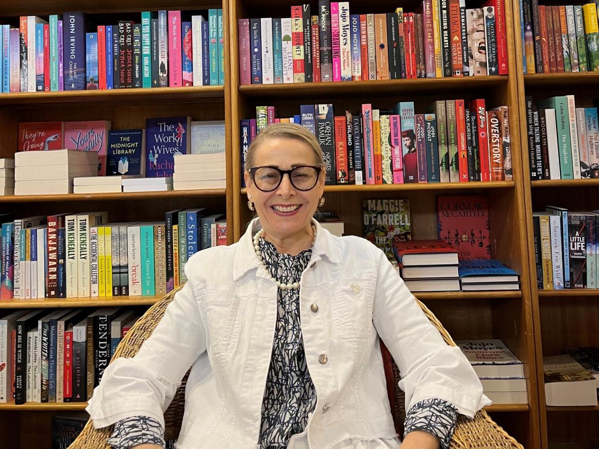 A portrait of Rachel smiling widely in front of a huge book case