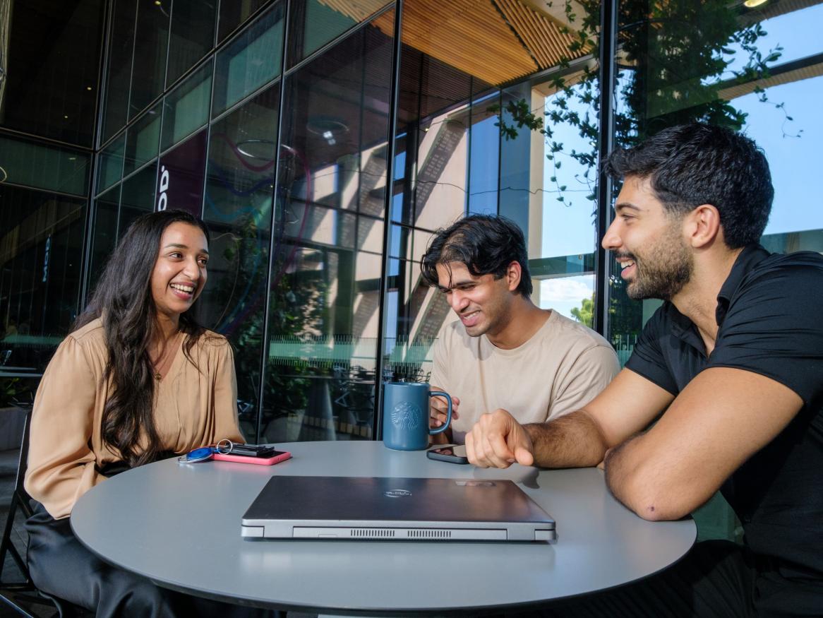 Three postgrads chatting at a table in a modern building 