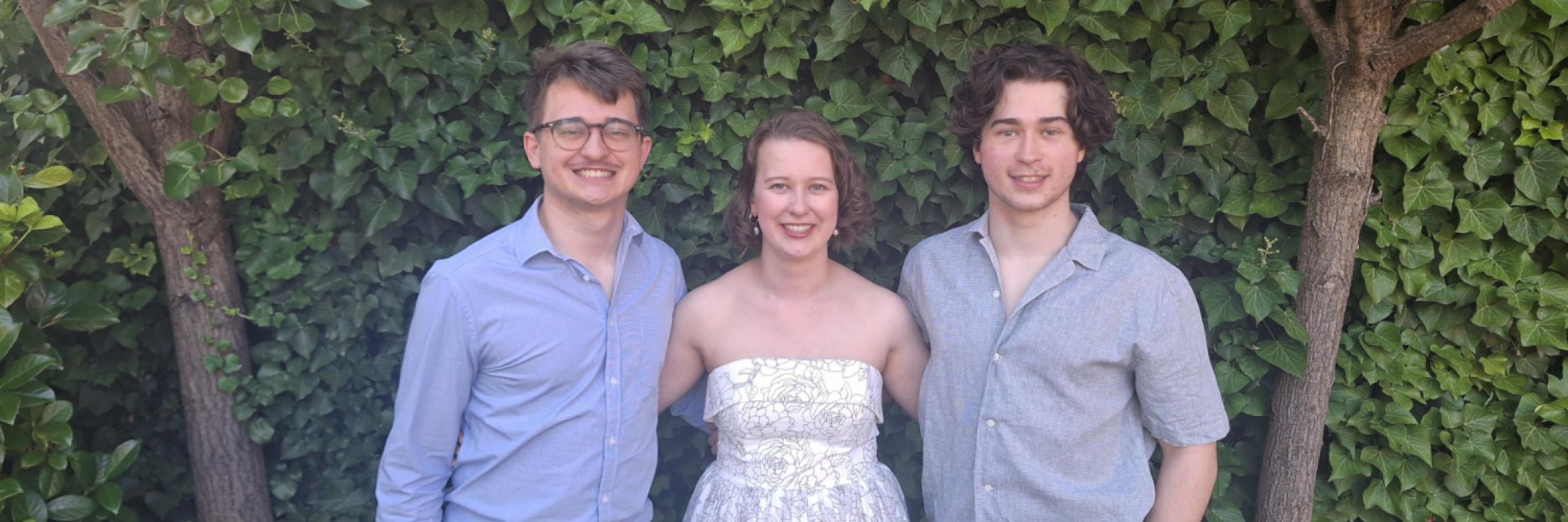 Three young adults standing together in front of a hedge