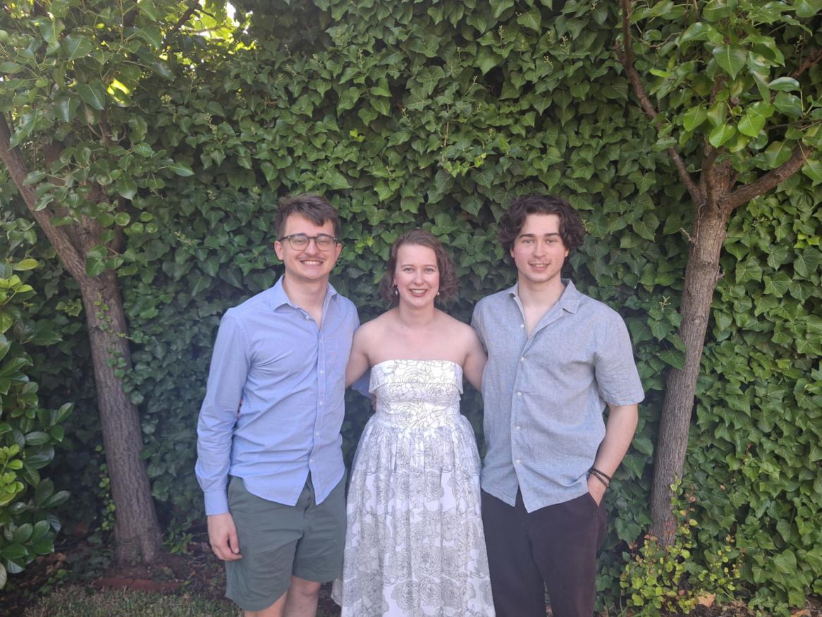 Three young  adults standing together in front of a hedge