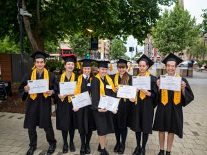 Students outside with graduation certificates