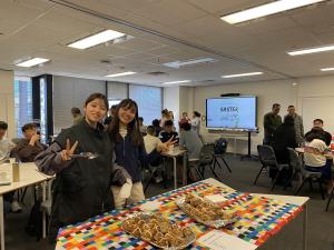 Landscape photo of various students in front of a table of Hot Cross Buns
