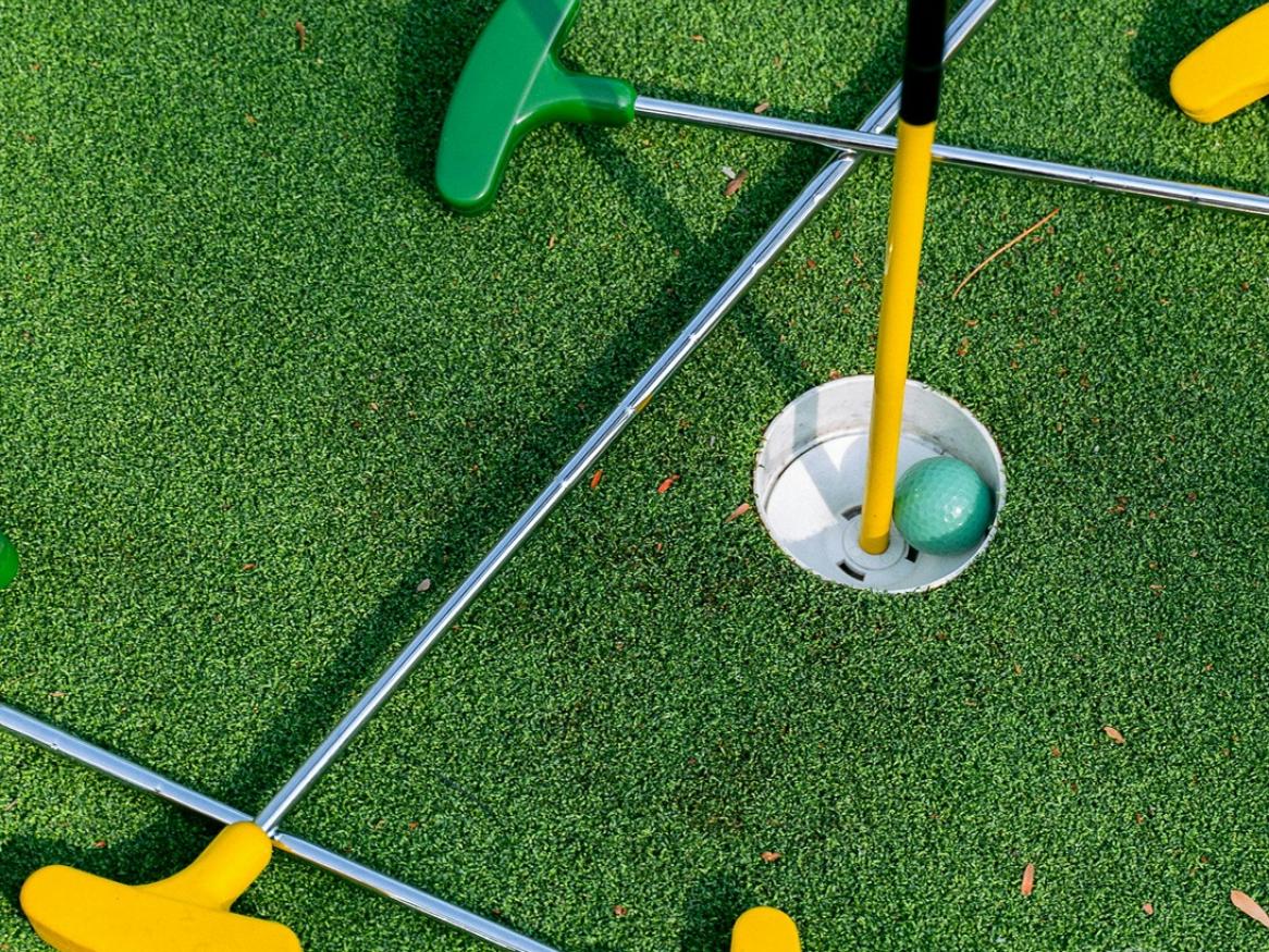 A pile of mini golf clubs and a hole with a mini golf ball in it
