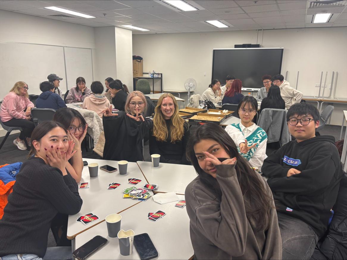 Landscape photo of ELC Students from Term 6 surrounding a table playing uno with pizza
