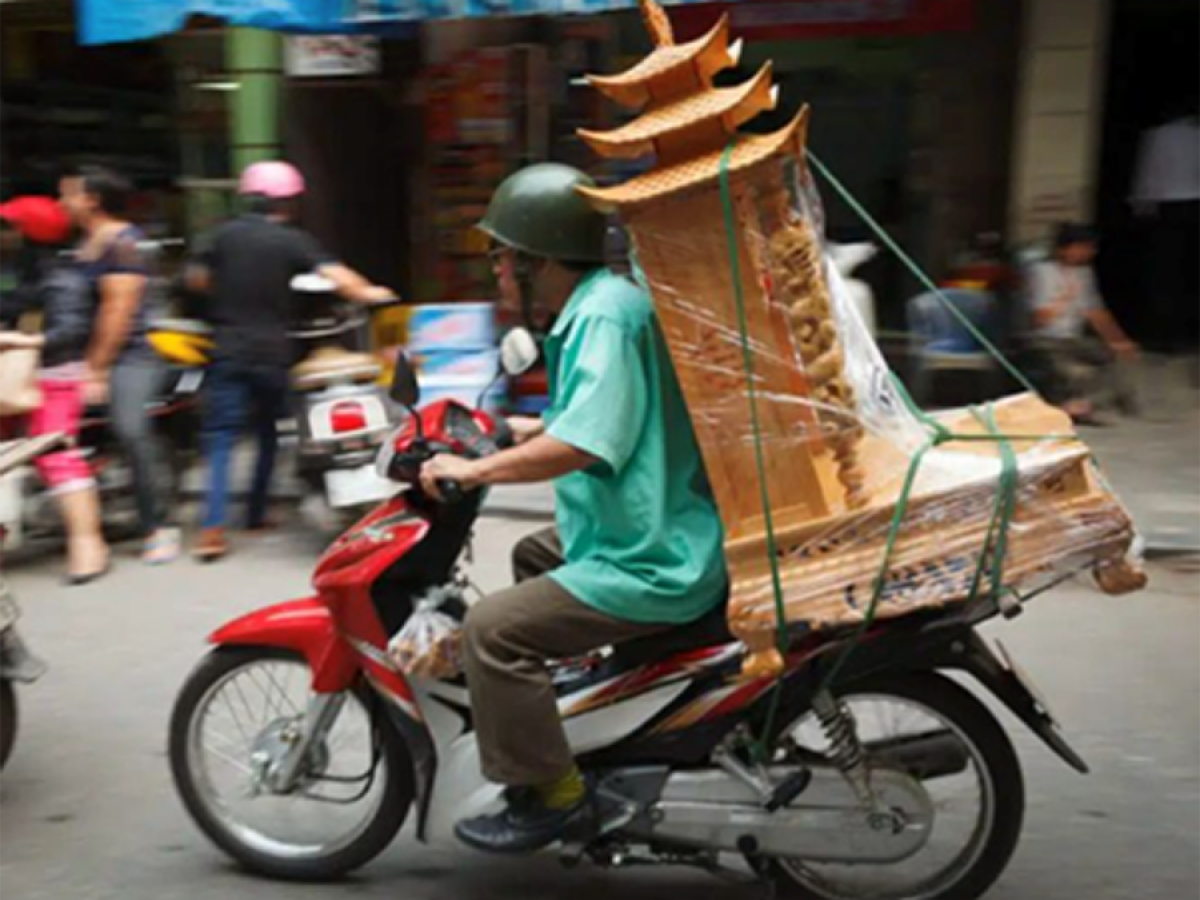 Man carrying timber furniture on the back of a motorbike in South East Asia.