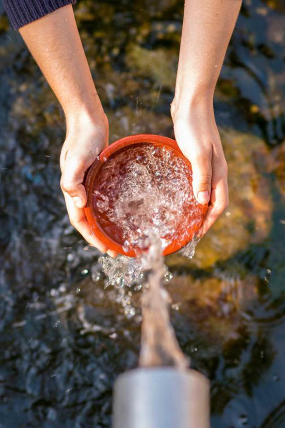 Water being filled into a container, top view, with two hands holding container