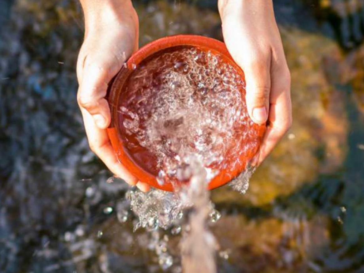 Water being filled into a container, top view, with two hands holding container