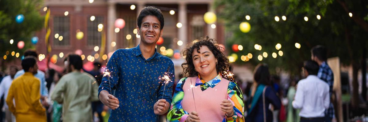 Two people standing in front of fairy lights holding sparklers