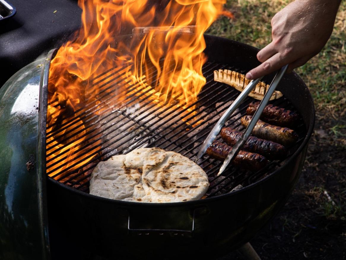 Sausages and bread are sitting on the grill of a barbecue