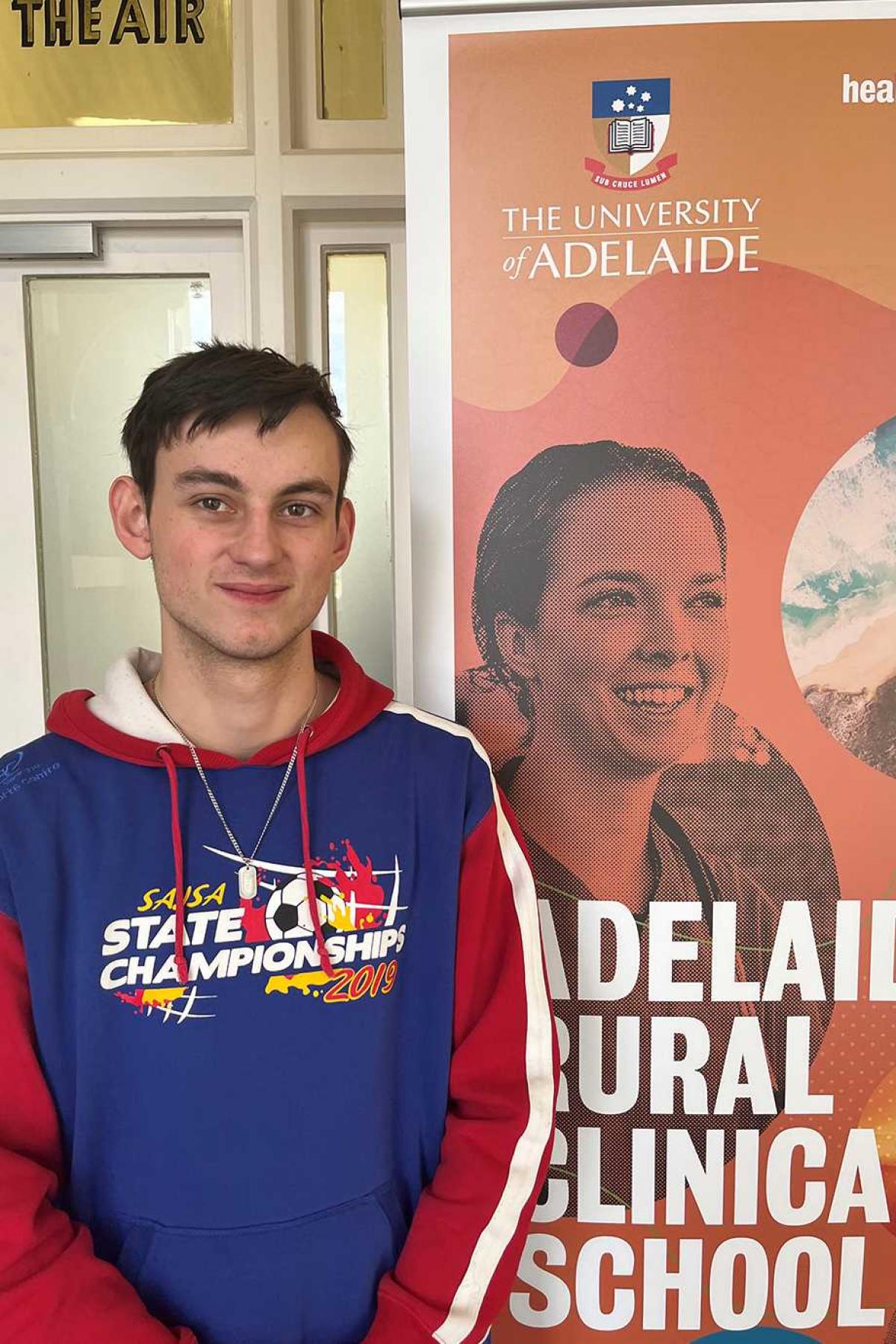 Tarran Dun standing next to Adelaide Rural Clinical School banner