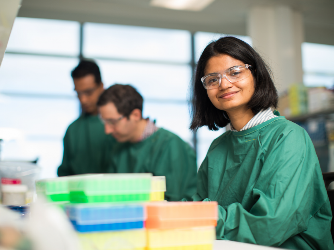 Researcher in lab wearing safety glasses and a green lab coat