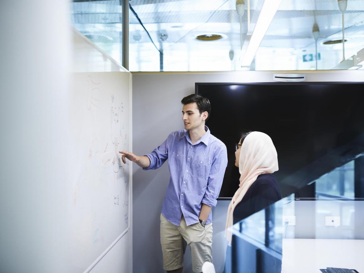 Two people inspect a whiteboard.