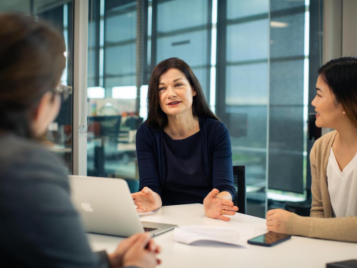 Three women talk at a desk.