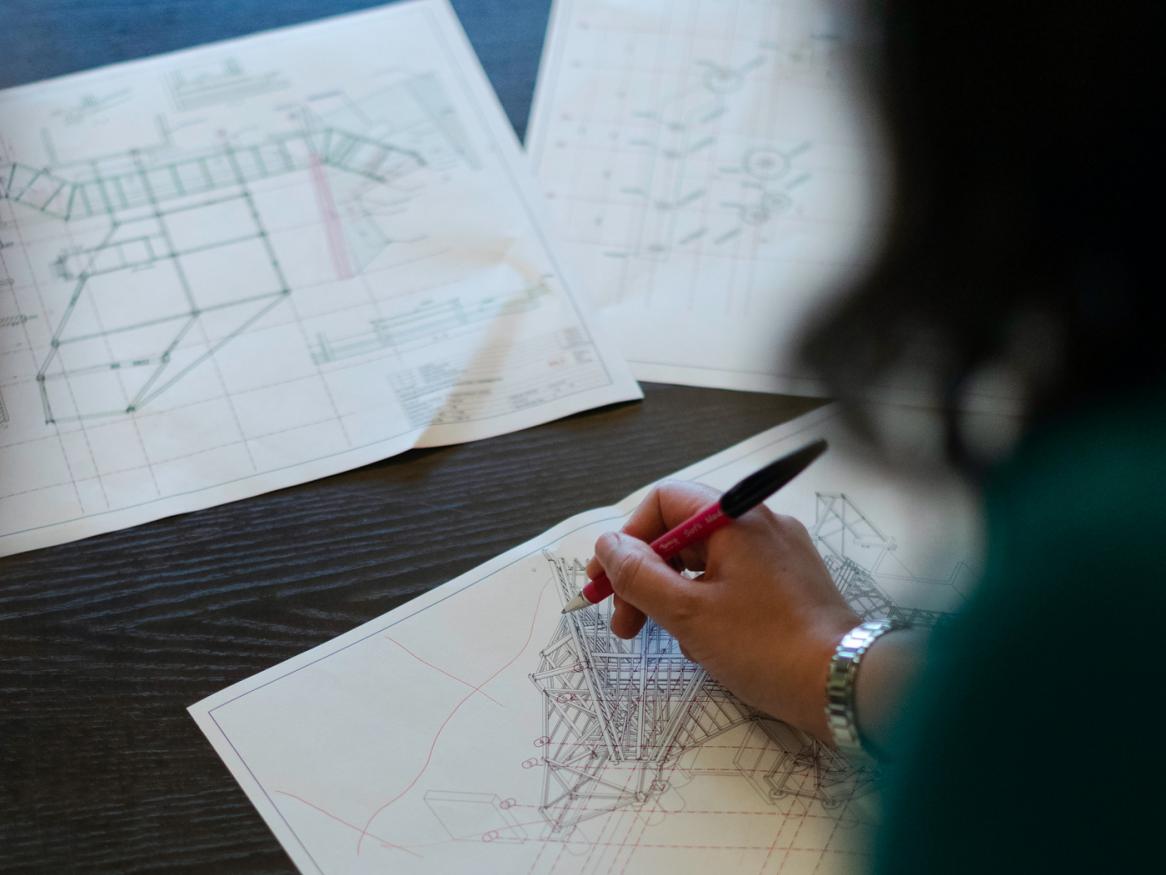 A woman in a green shirt draws on some plans.