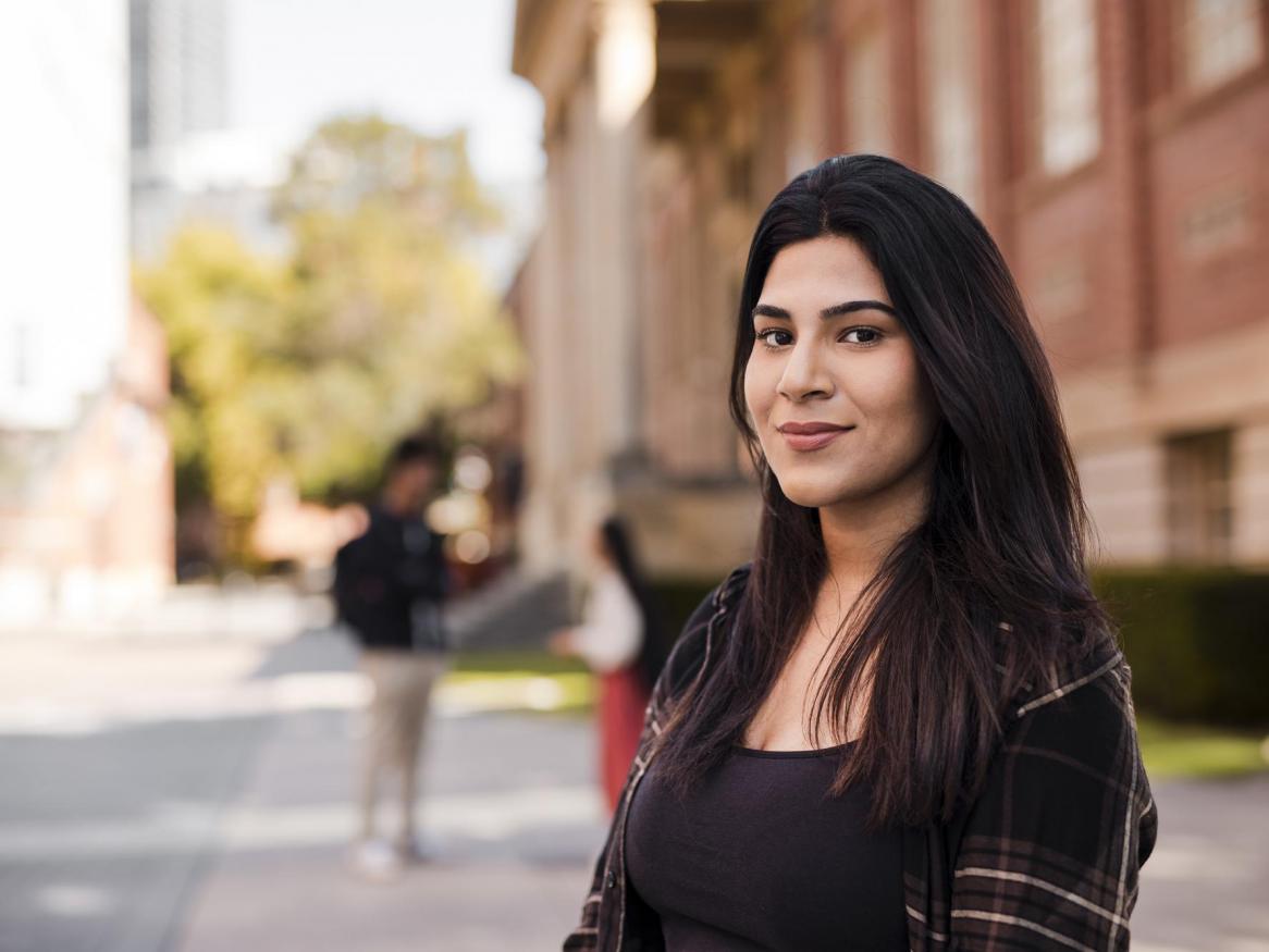 A student looks at the camera, with the University of Adelaide's Barr Smith Library in the background.