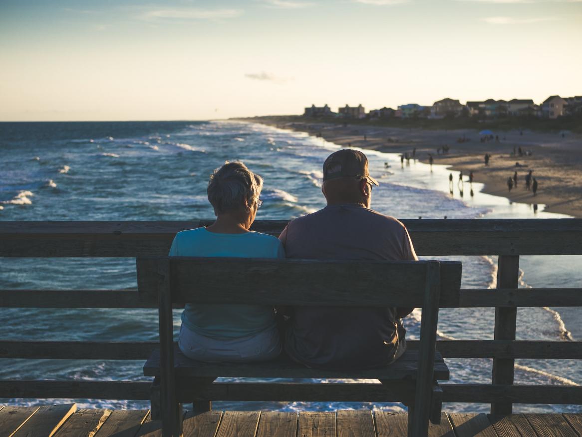 A man and woman sitting on a jetty looking towards the beach
