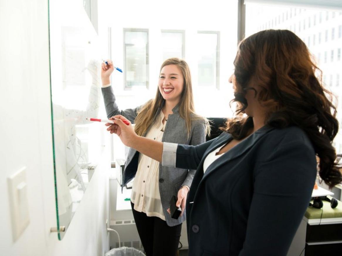 Two women writing on a whiteboard