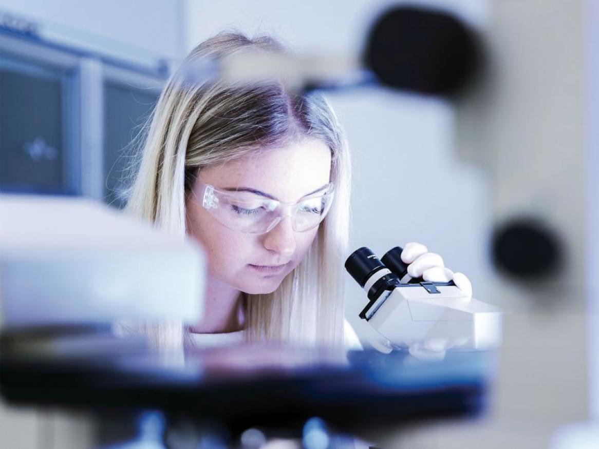 A photo of a girl looking at a research lab looking through a microscope