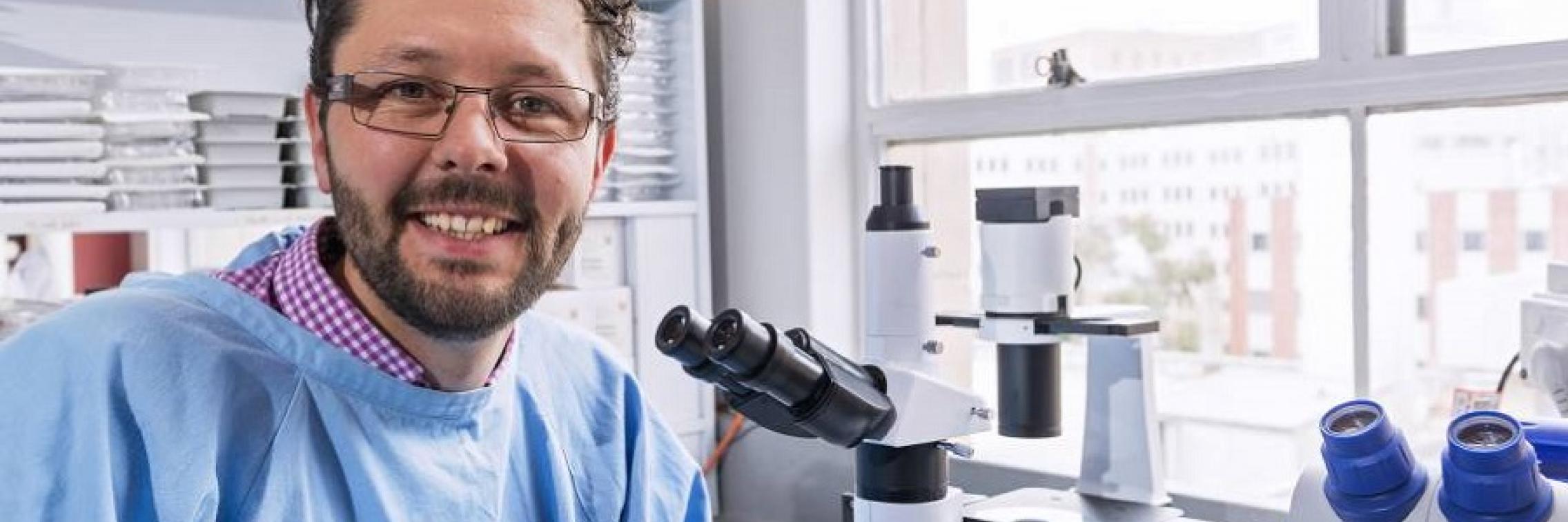 Prof Mark Hutchinson in lab coat in front of microscope