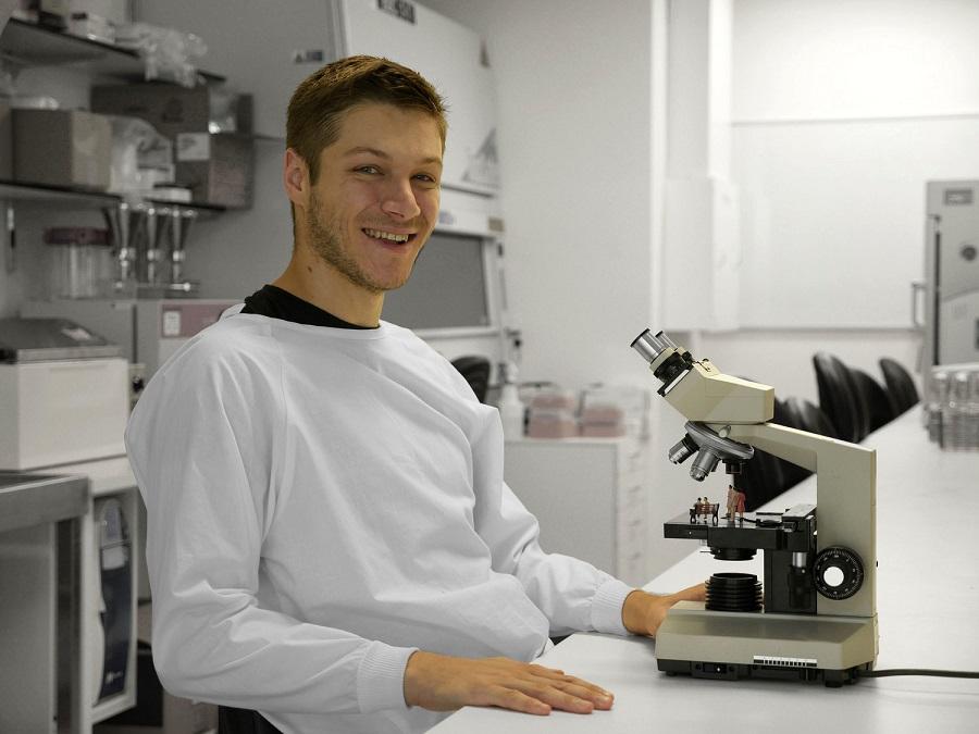 Matthew Briggs in lab coat in front of microscope