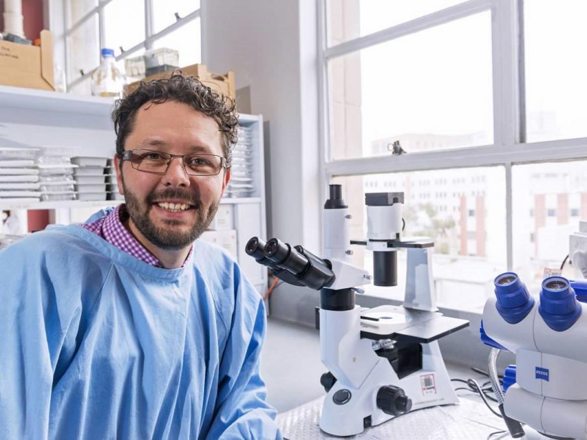 Prof Mark Hutchinson in lab coat in front of microscope