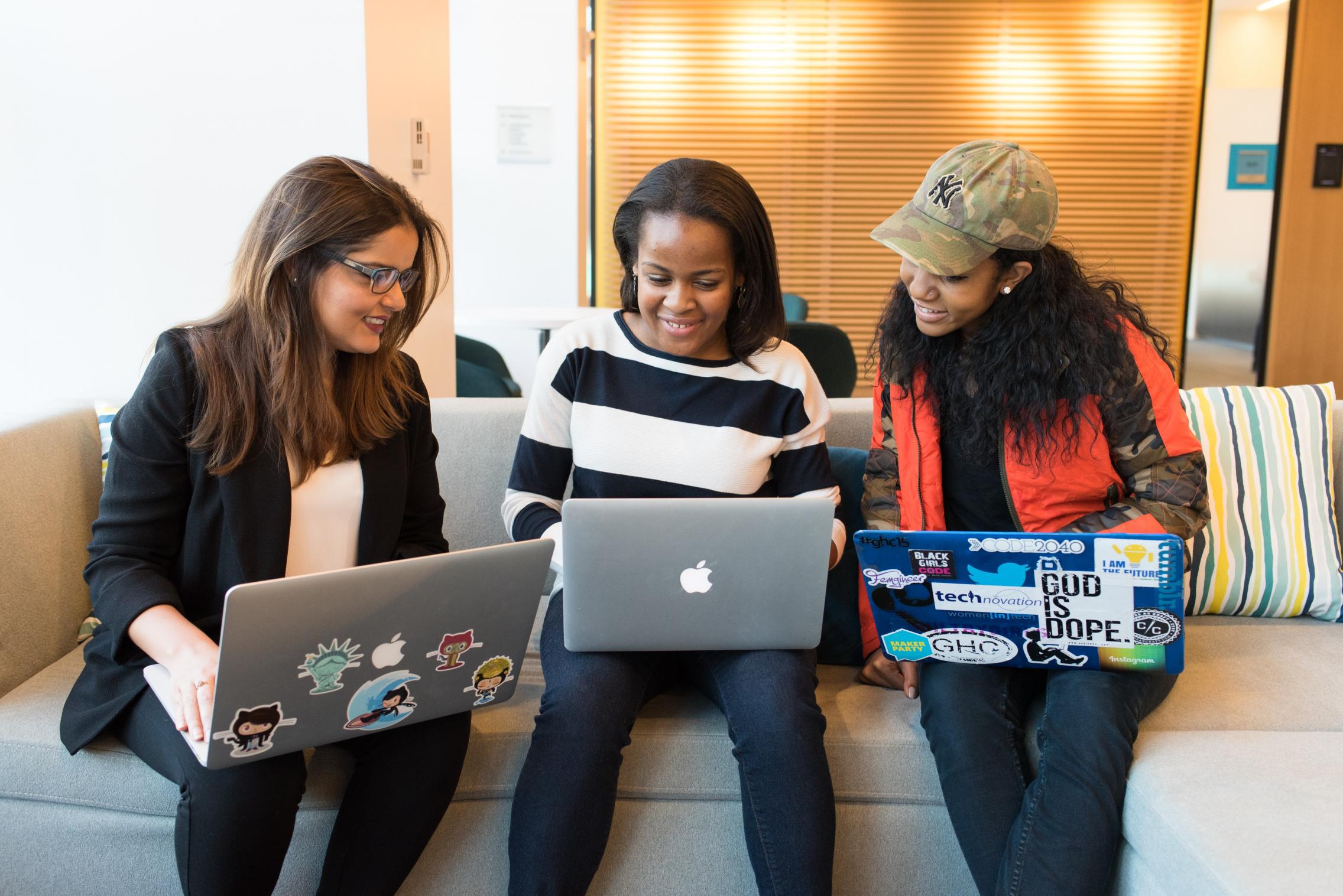 Three women sitting on a couch with their laptops