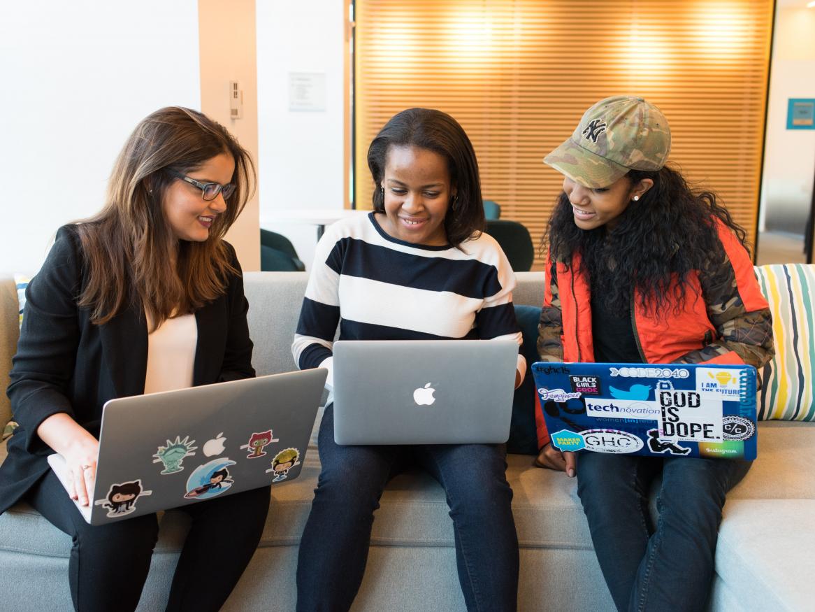 Three women sitting on a couch with their laptops