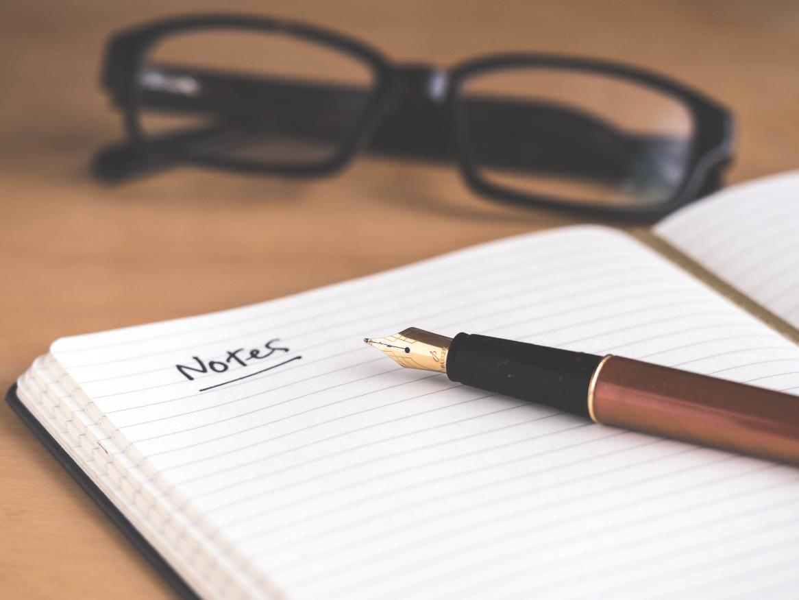 A notebook, a pen and glasses on a table